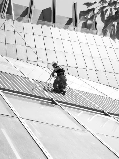 our-story Deux employés nettoient les vitres d’une façade vitrée à l’aide d’une nacelle, pour améliorer l’apparence du bâtiment.