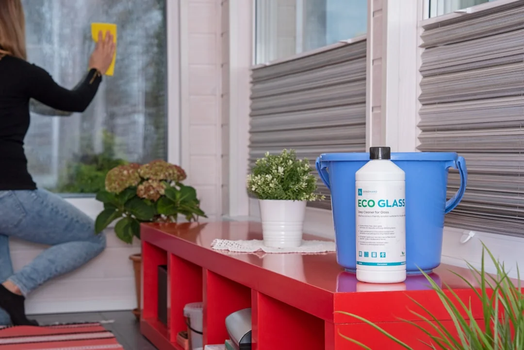 A man outdoors cleaning a glass barrier with a squeegee, with greenery all around.
